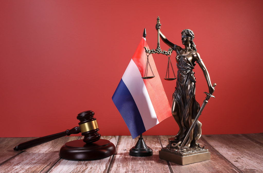 Statue of Lady Justice with Judge gavel and flag of Netherlands