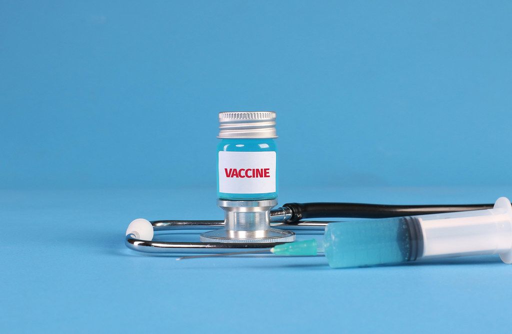 Stethoscope and bottle with vaccine on blue background