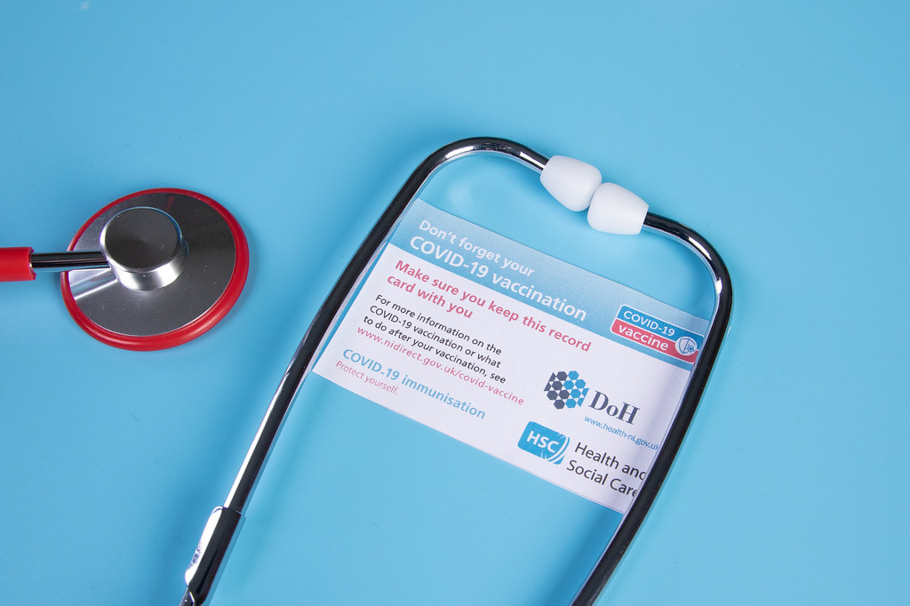 Stethoscope and Covid-19 vaccination record card on blue background