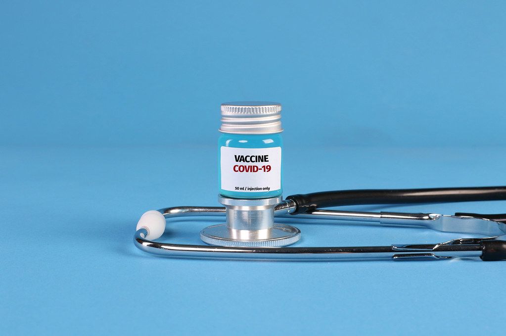 Stethoscope and Covid-19 vaccine on blue background