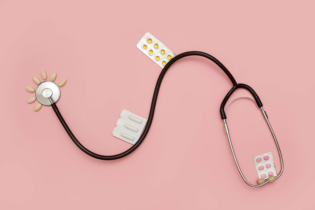 Stethoscope and medicines on bright pink background