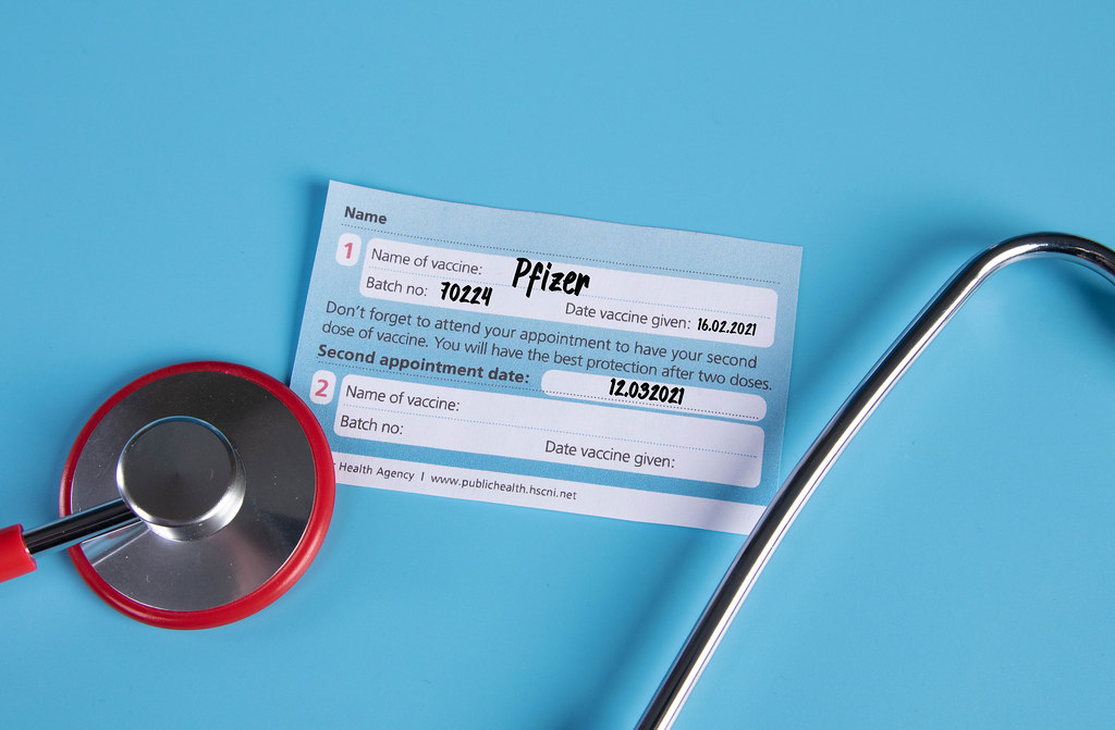 Stethoscope and Pfizer Covid-19 vaccination certificate on blue background
