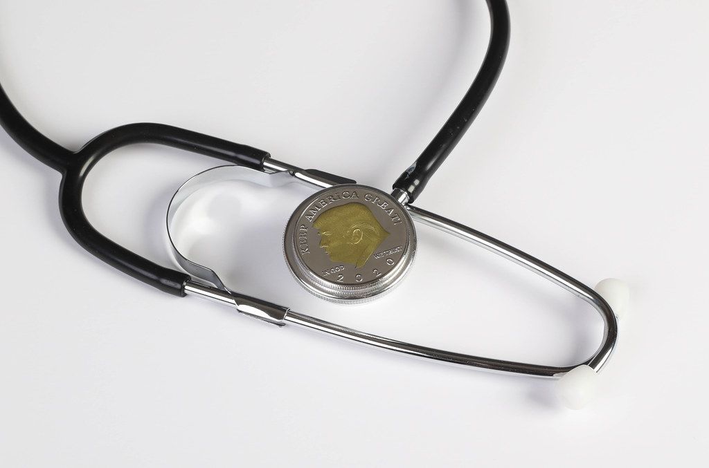 Stethoscope and silver coin with Donald Trump on white background