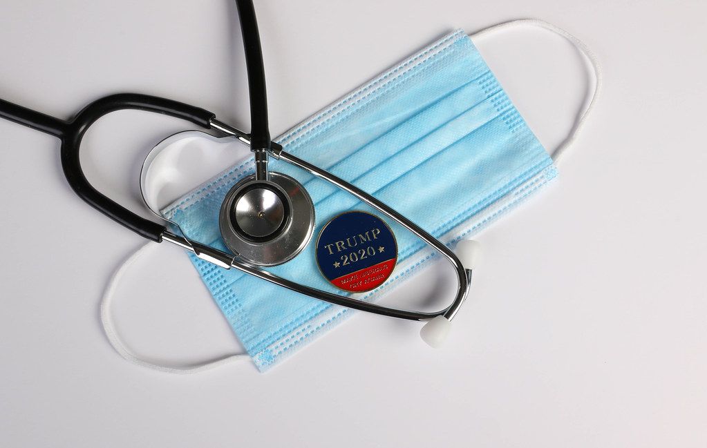 Stethoscope, face mask and coin with Trump 2020 text on white background
