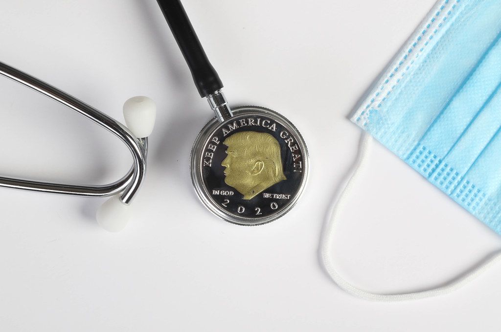 Stethoscope, face mask and silver coin with Donald Trump on white background