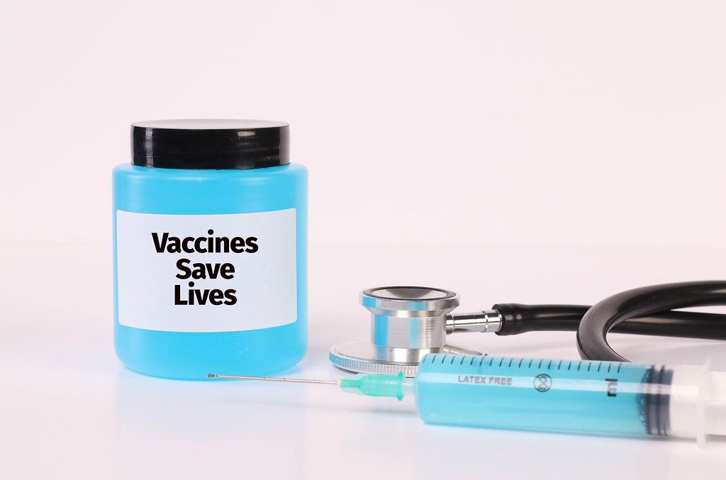 Stethoscope, syringe and bottle with blue fluid and Vaccines Save Lives text