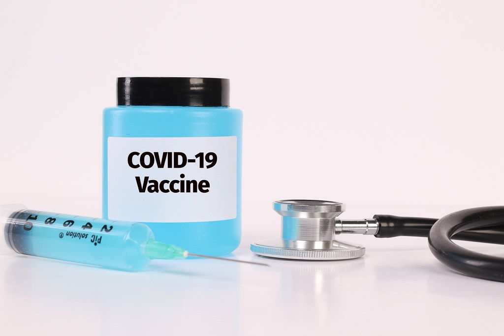 Stethoscope, syringe and bottle with Covid-19 Vaccine text on white background