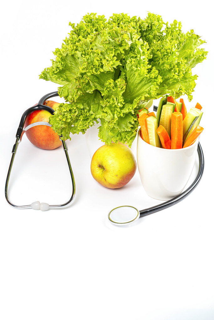 Stethoscope with fresh apples, carrots, cucumber and lettuce