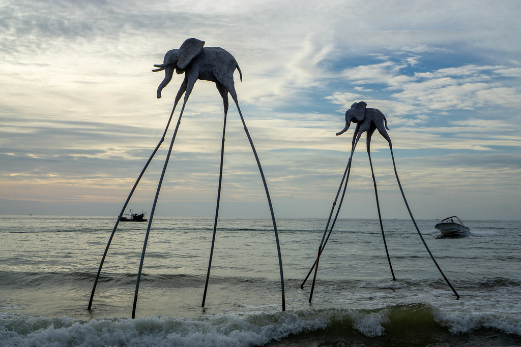 Sunset Photo of Elephant Sculptures on Long Sticks with Fisherboat and Motorboat in the Background at Sunset Sanato Beach Club on Phu Quoc Island in Vietnam