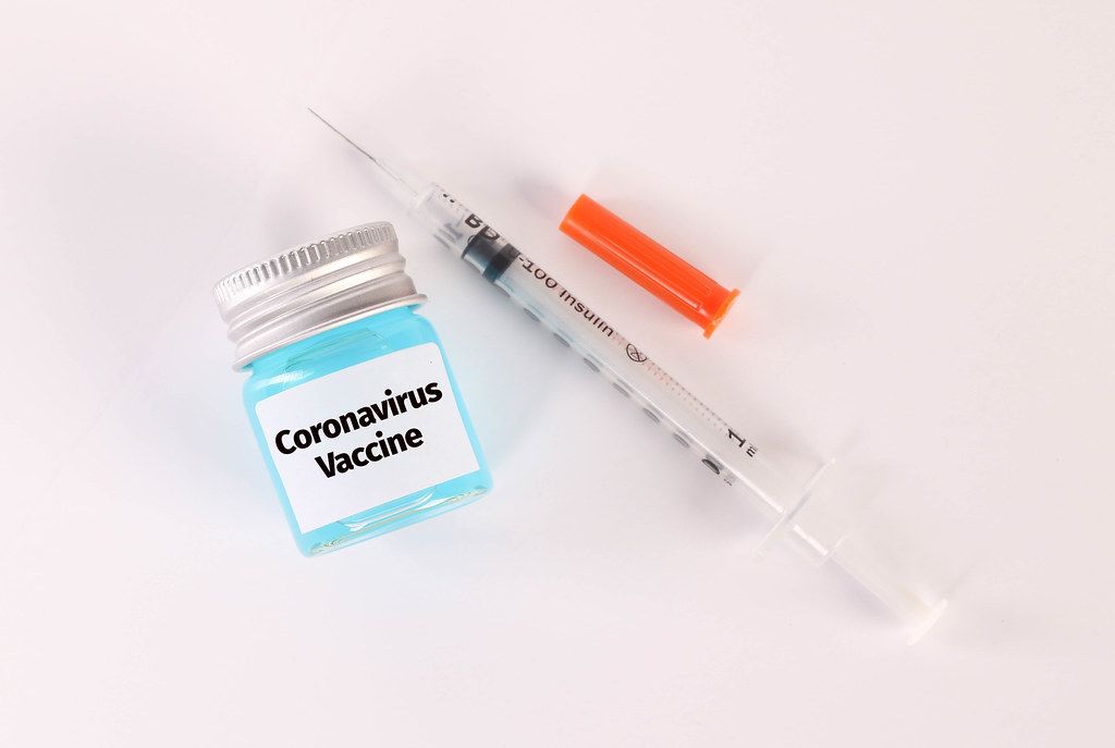 Syringe and bottle with blue fluid and Coronavirus Vaccine text on white background