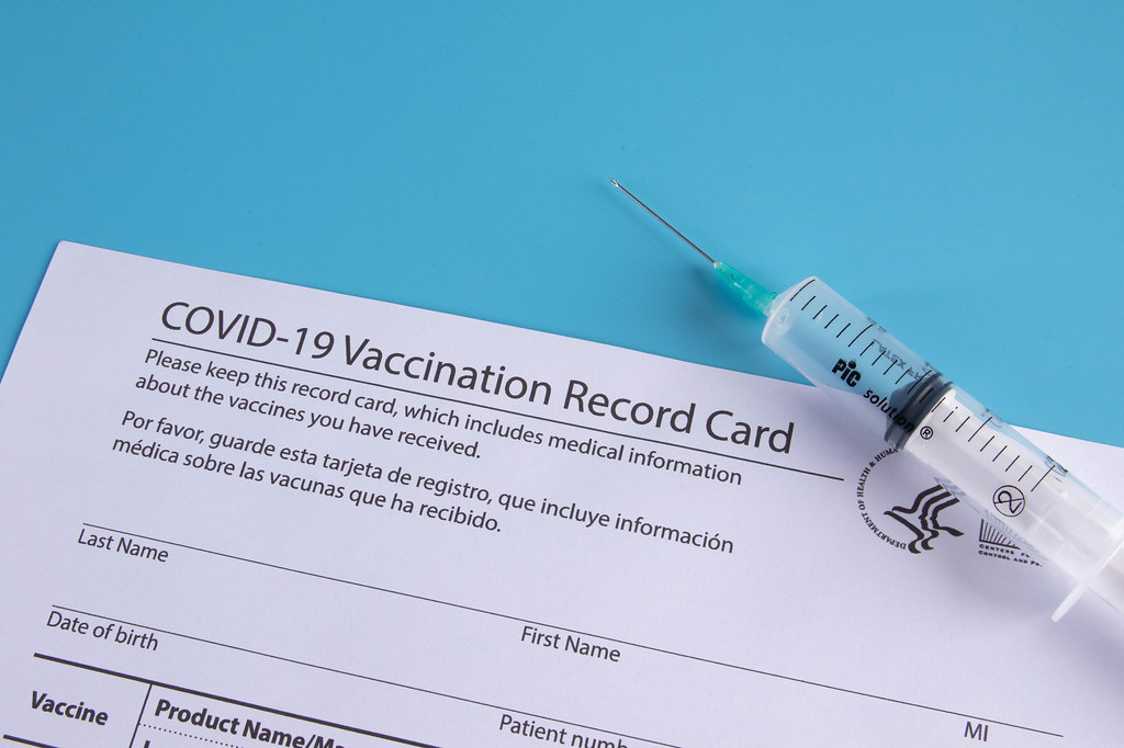 Syringe and vaccination record card on blue background