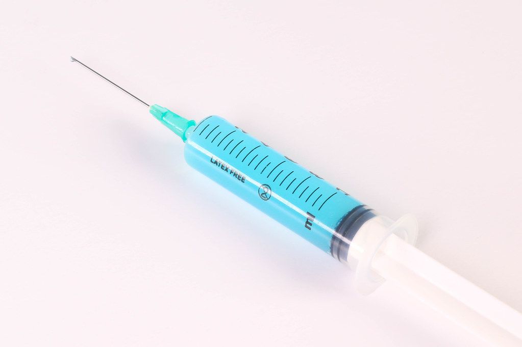 Syringe with blue fluid on white background