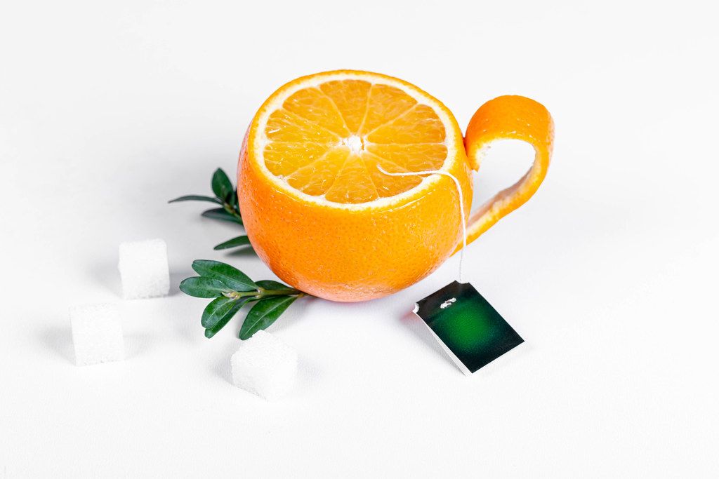Tea party concept. Orange cup with sugar and green leaves on white