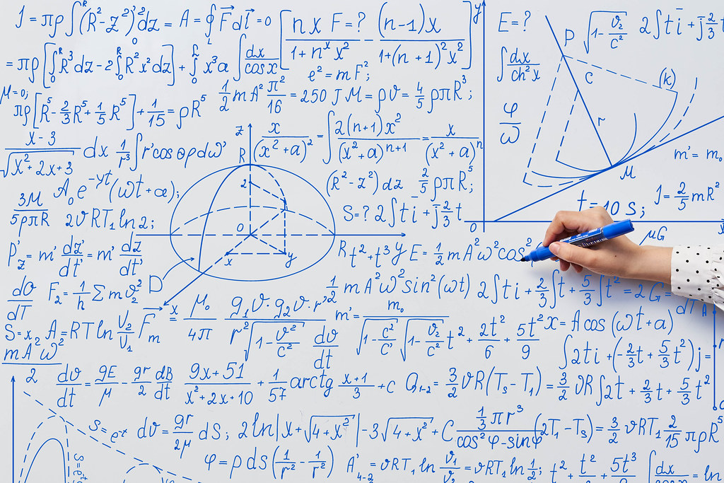 Teacher's hand writing complicated mathematical formulas on the whiteboard