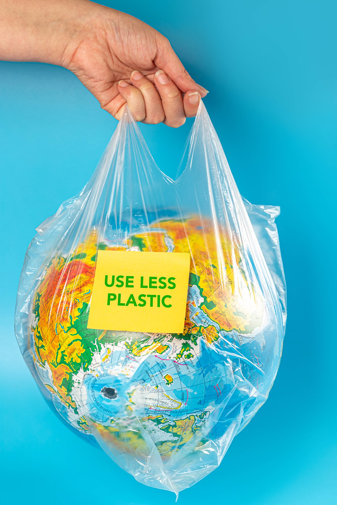 The concept of earth day. The women hand holds the earth in a plastic bag with inscription use less plastic, blue background