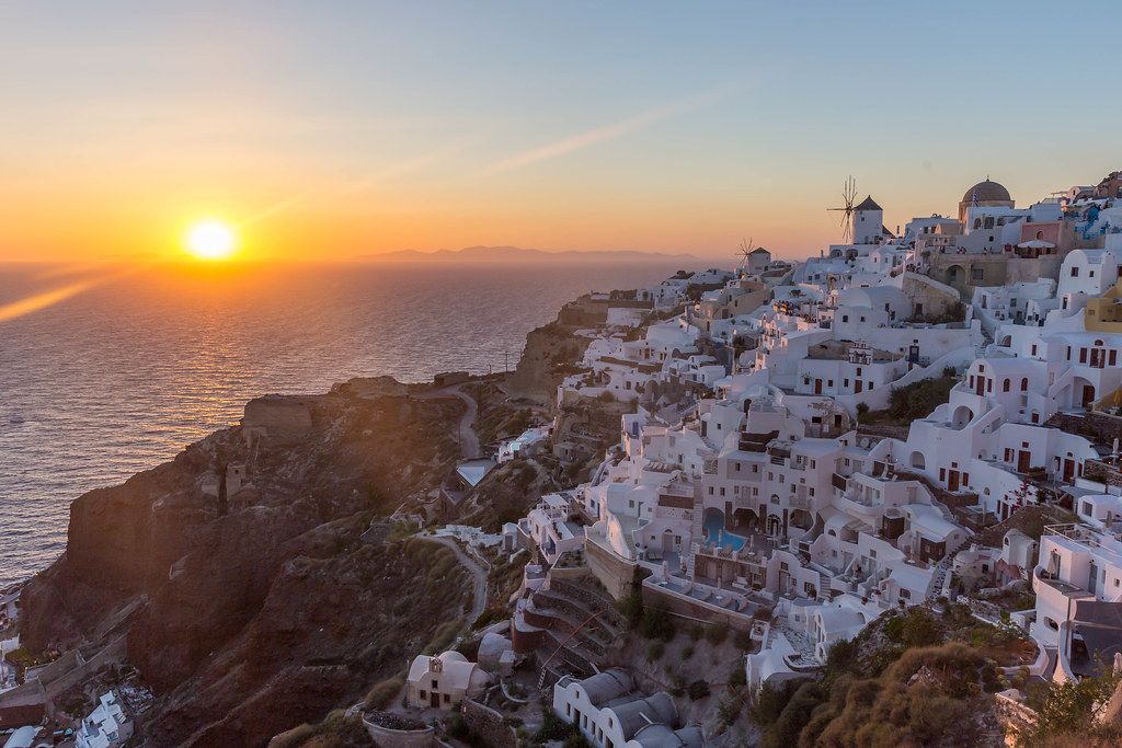 The sun sets on the Aegean Sea and the white houses of Oia shine in a light pink hue. A must see