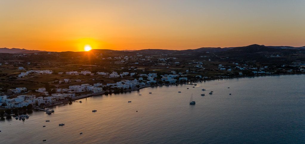 The sun sets on the island of Milos, South Aegean. Aerial photo with boats and the town of Adámas