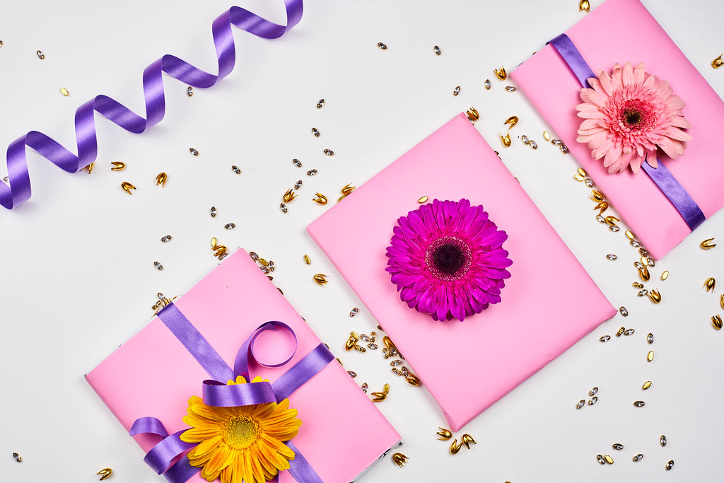 Three gifts with pink wrapping paper, purple ribbon and flowers. Background with golden decoration