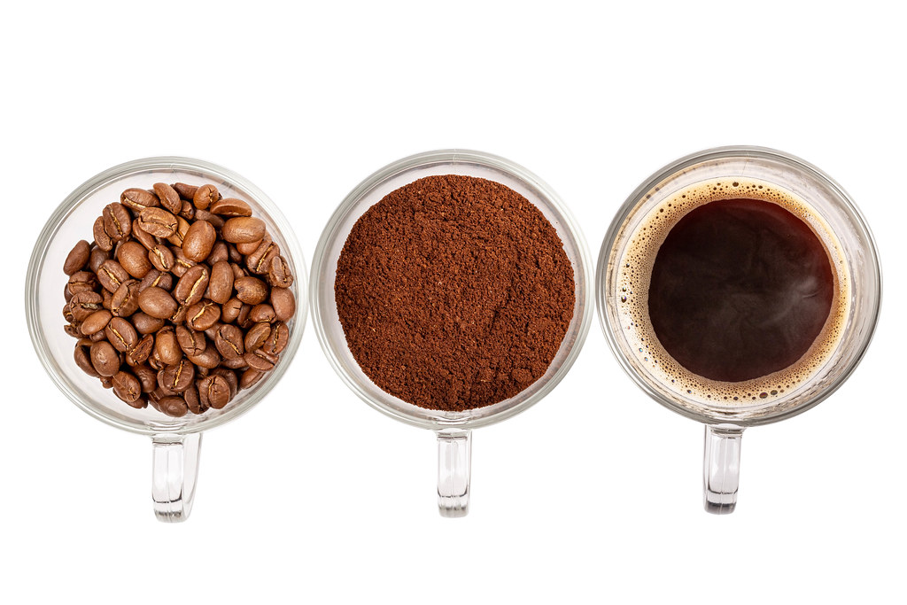 Three glass cups with prepared coffee, whole grains and ground coffee on a white background, top view