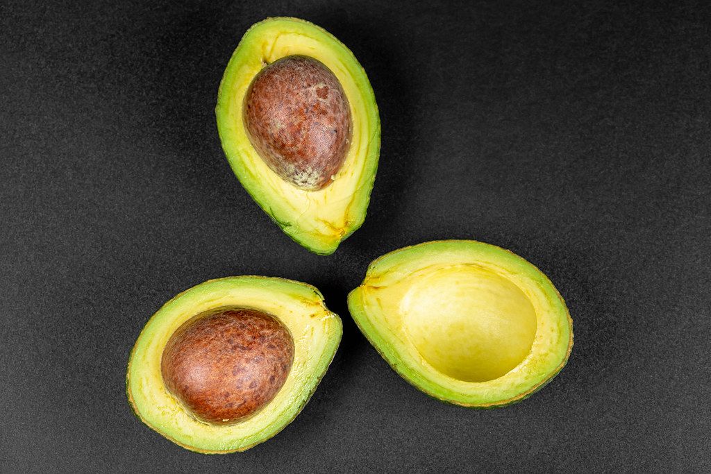 Three halves of an avocado on a black background, top view