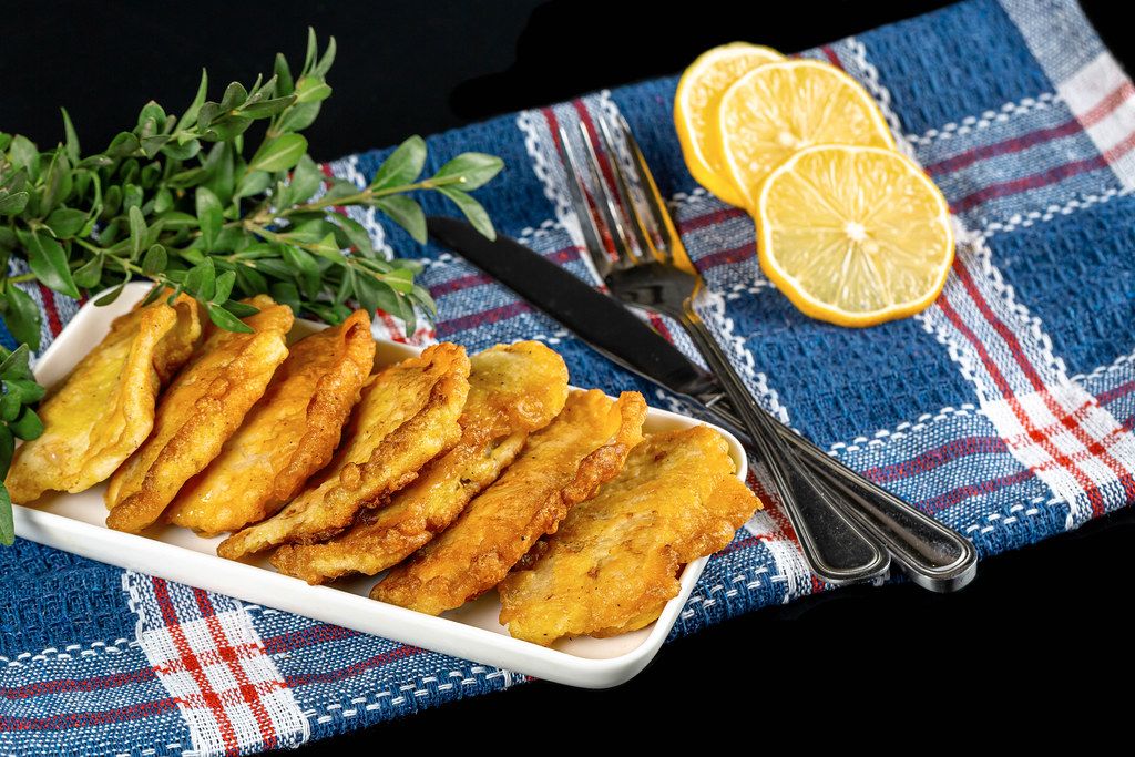 Tilapia fried pieces on a white plate with a knife and fork