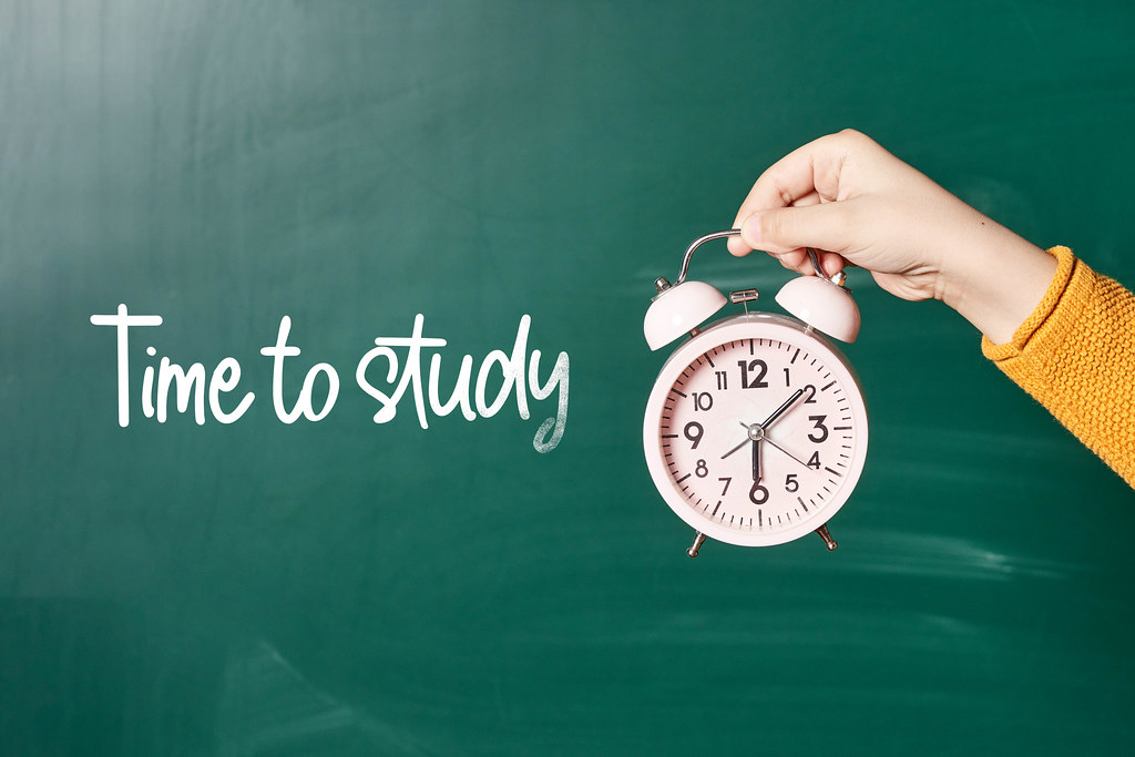 Time to study text on chalkboard and hand holding alarm clock