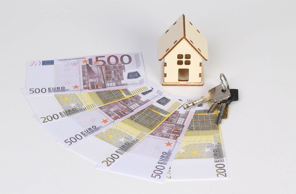Tiny wooden house with keys and Euro banknotes on white background