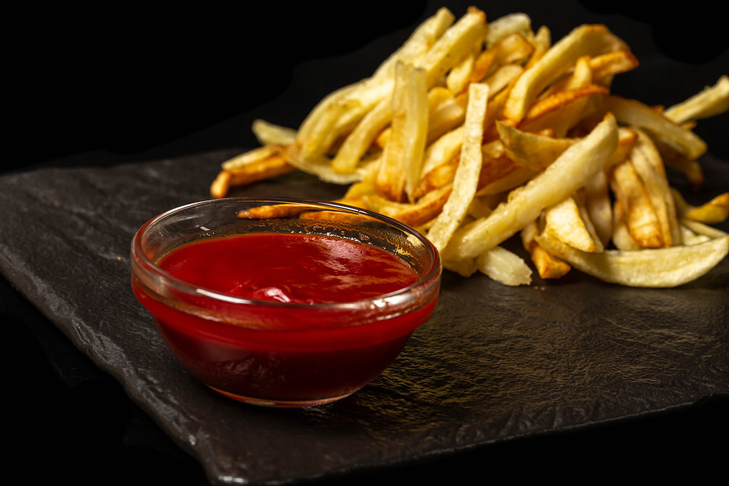 Tomato sauce and fried fries on black background