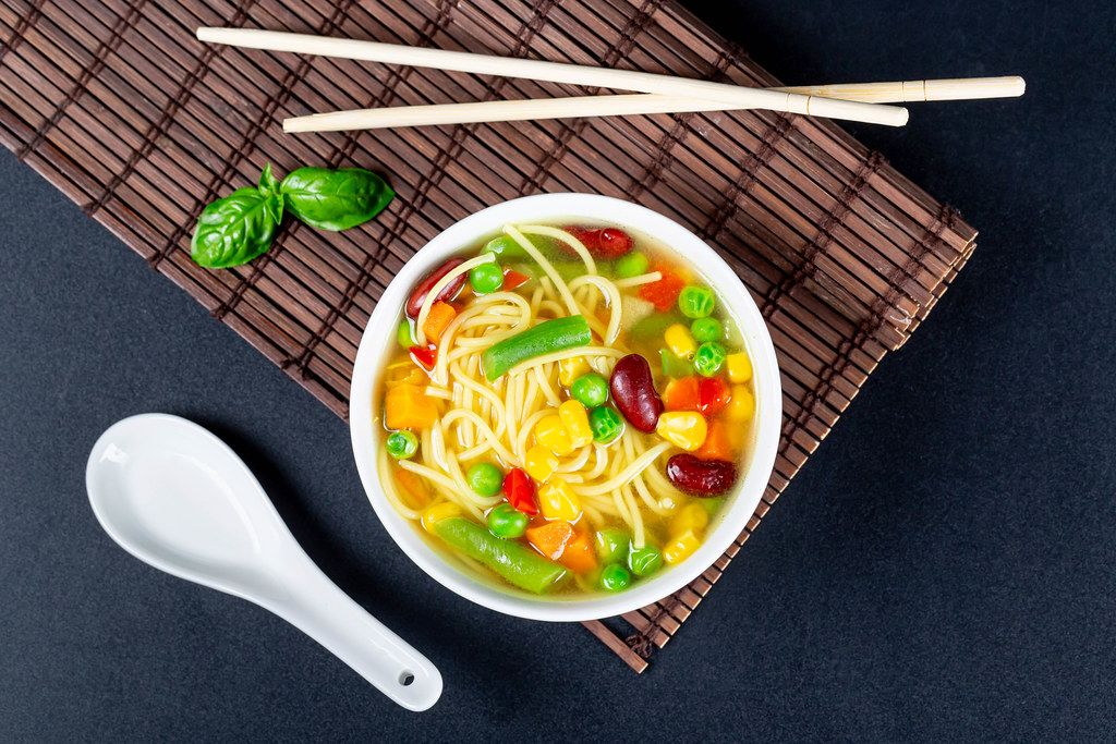 Top view, a bowl of vegetable soup with chopsticks and a spoon