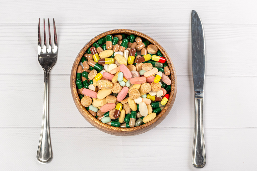 Top view, a bowl with colorful capsules and tablets on a wooden background with a knife and fork