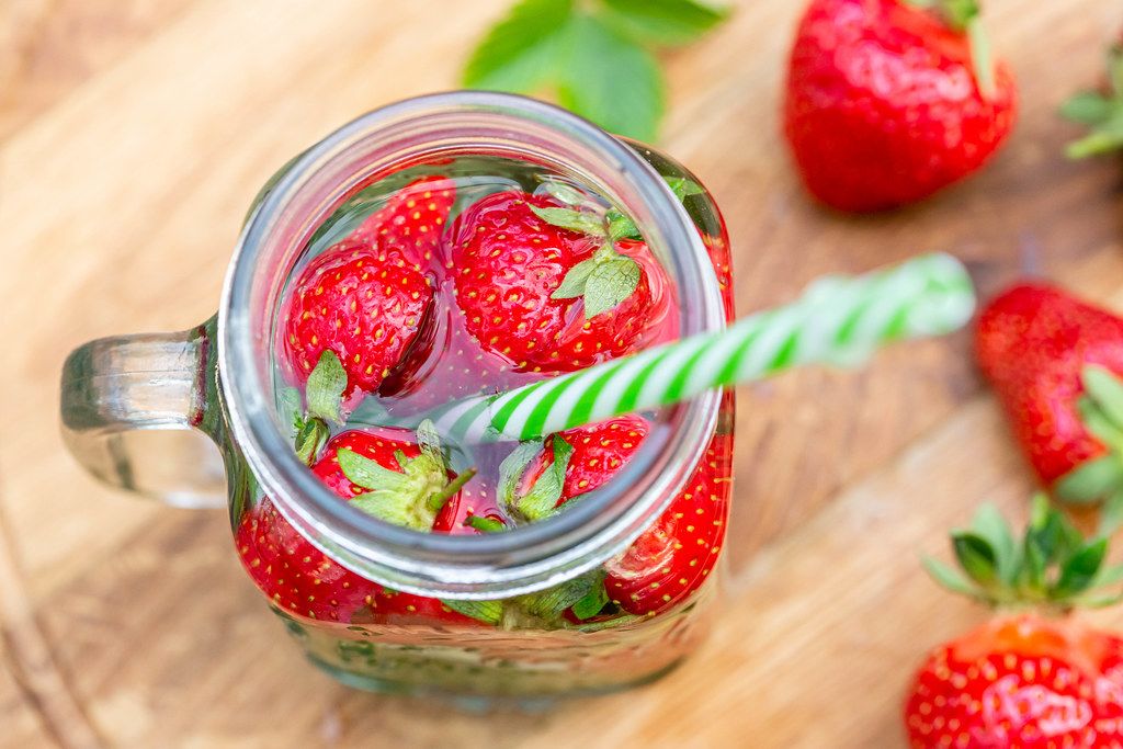 Top view, a jar of strawberry drink and a straw on wooden background