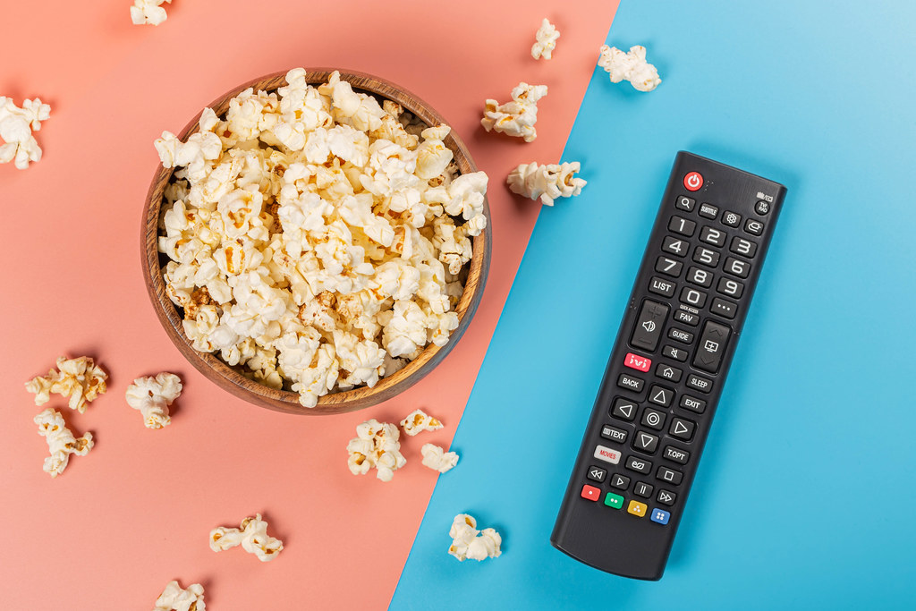 Top view, bowl of popcorn with tv remote control on pink and blue background