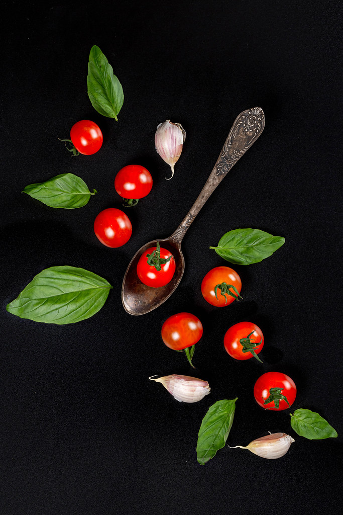 Top view, cherry tomatoes, garlic and basil leaves on a black background