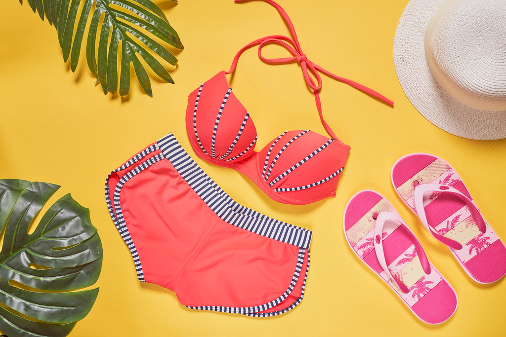 Top view female summer beach bikini, straw hat, flip flops and on yellow