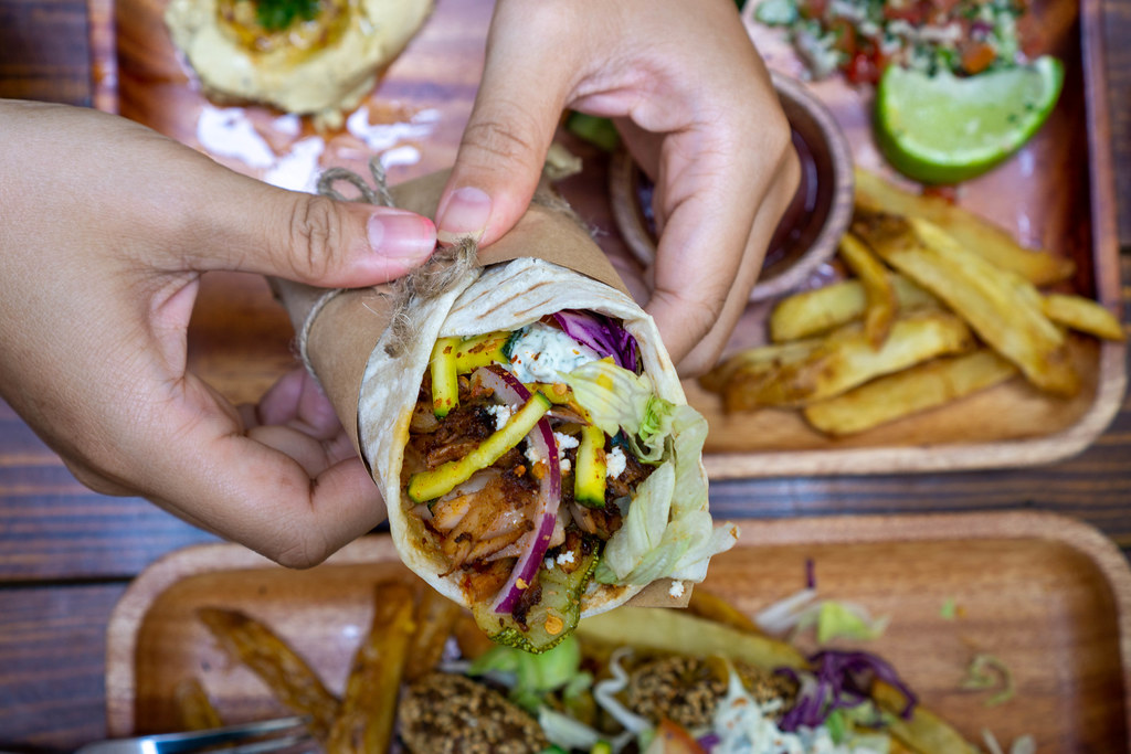 Top View Food Photo of Person holding Doner Durum Kebab Roll with Chicken Meat, Fresh Vegetables and Tzatziki Sauce with both Hands