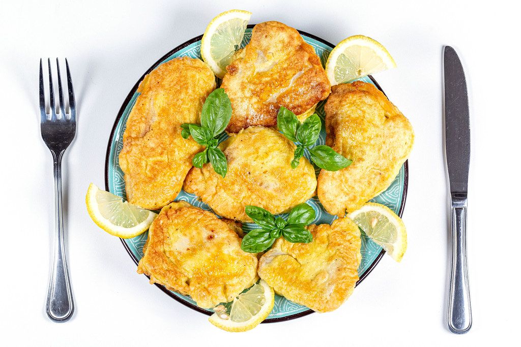 Top view, fried tilapia in batter on a plate with basil leaves and lemon slices
