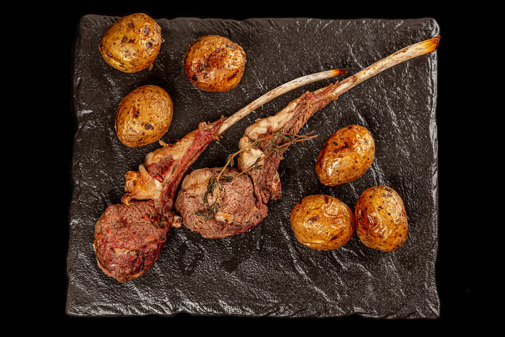 Top view, grilled lamb ribs and potatoes with thyme on dark background