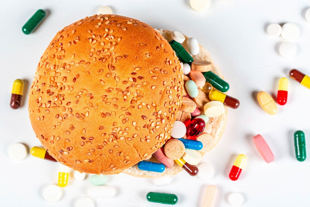Top view of burger and medical pills and capsules on white background