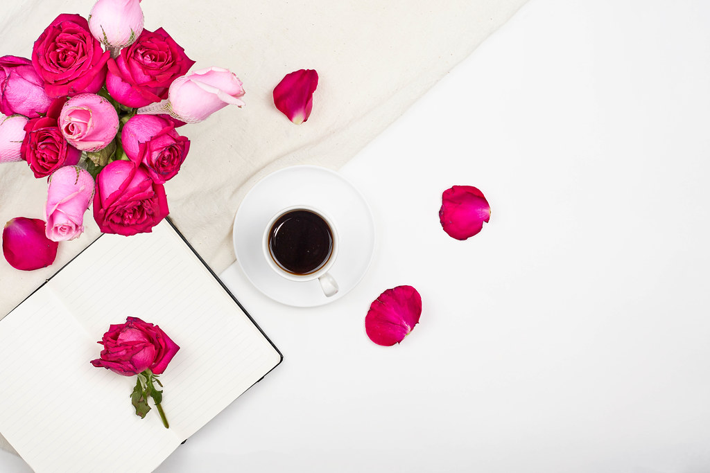 Top view of creative woman's desktop with open notepad, coffee cup and rose flowers