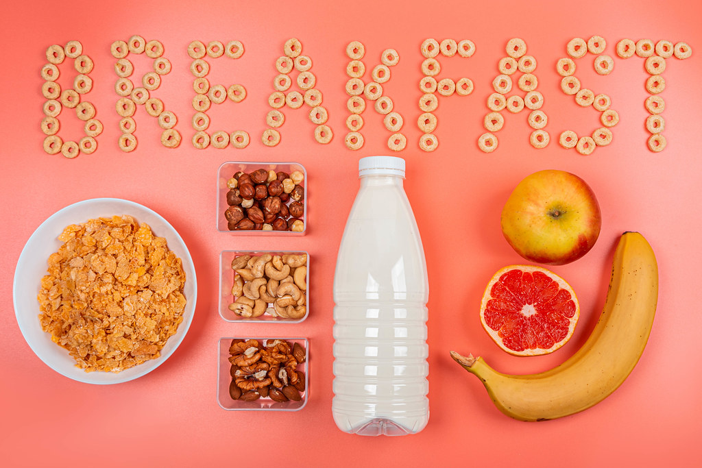 Top view of nuts, fruits, milk and cornflakes on pink background with word breakfast