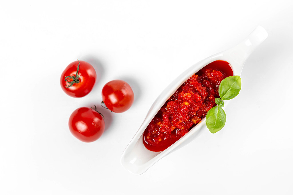 Top view of tomato sauce and fresh cherry tomatoes on white background