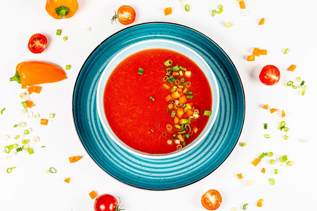 Top view of tomato soup with herbs and bell pepper on a white background