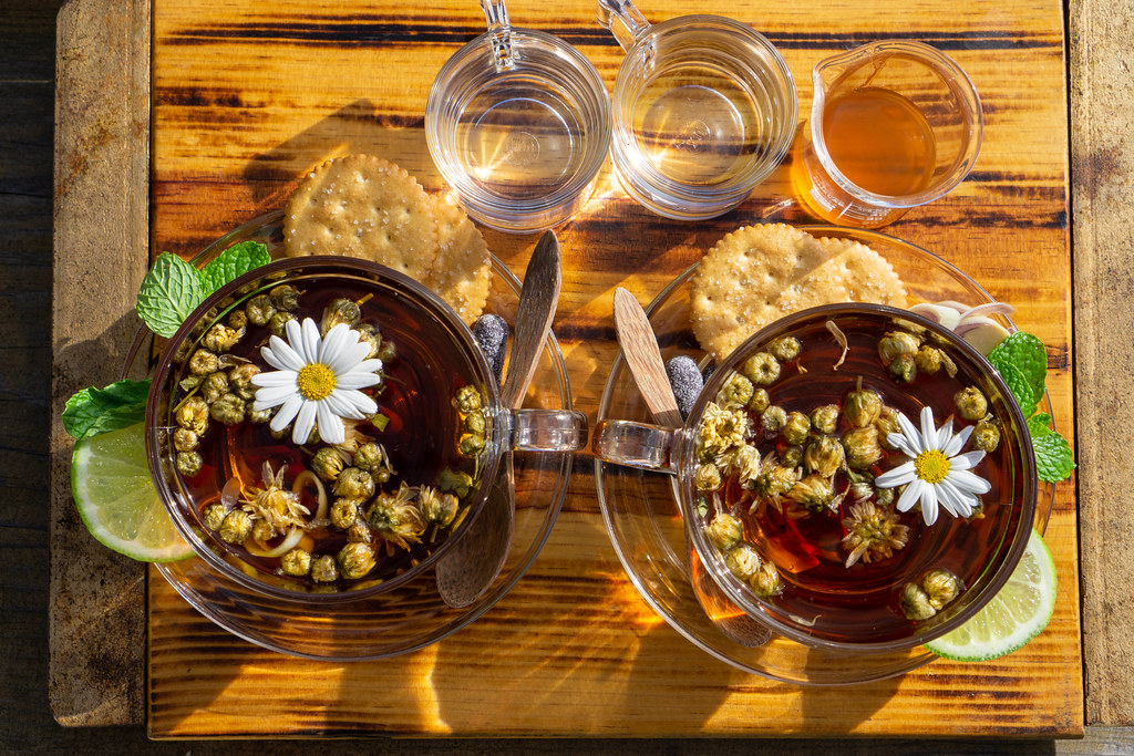 Top View Photo of Chamomile Tea in Glass Mugs with Lemongrass, Lemon, Mint, Cookies, Syrup and Honey on a Wooden Tray with Wooden Spoons