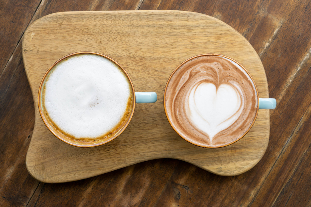 Top View Photo of Two Ceramic Cups of Hot Chocolate and Cappuccino with Heart Shaped Latte Art on a Wooden Board