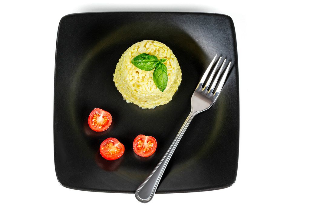 Top view, rice with tomatoes and basil in a black plate on a white background