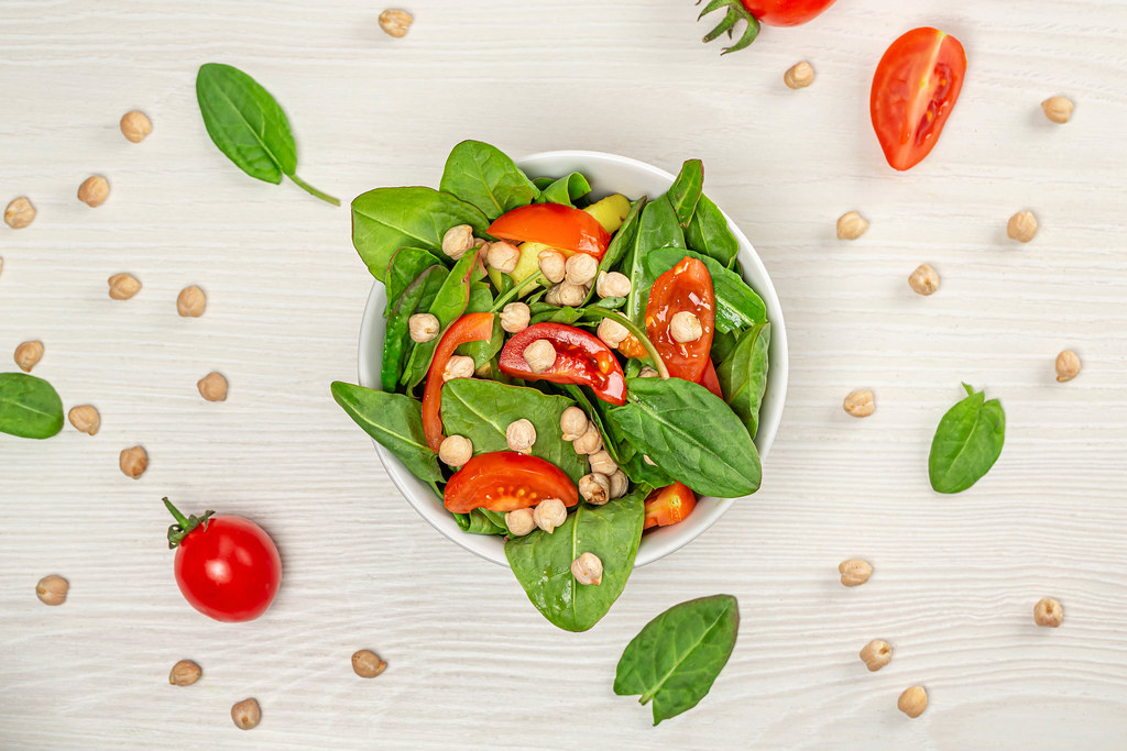 Top view salad with chickpeas and tomatoes on white wooden background
