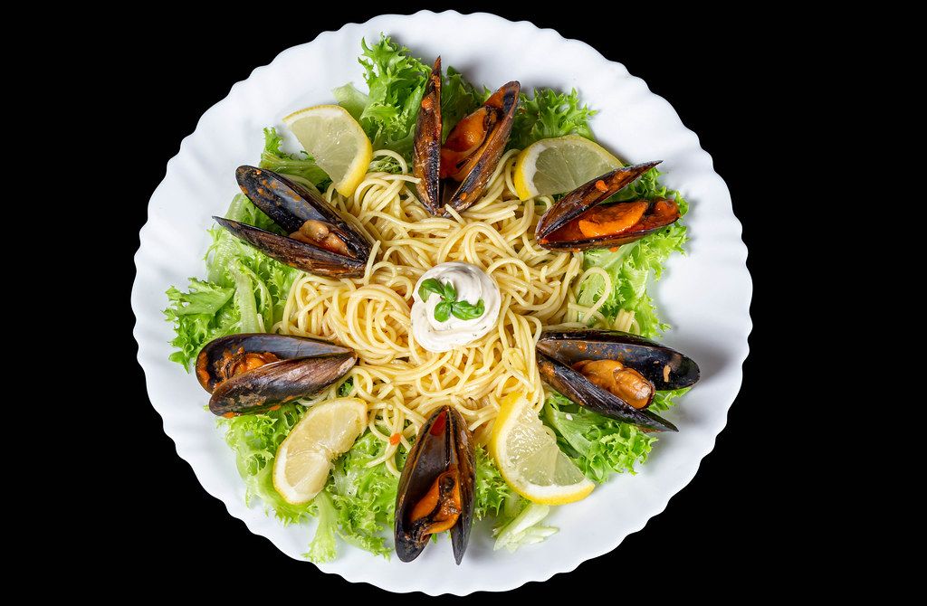 Top view, spaghetti with mussels, lettuce, lemon slices and cheese sauce on a black background