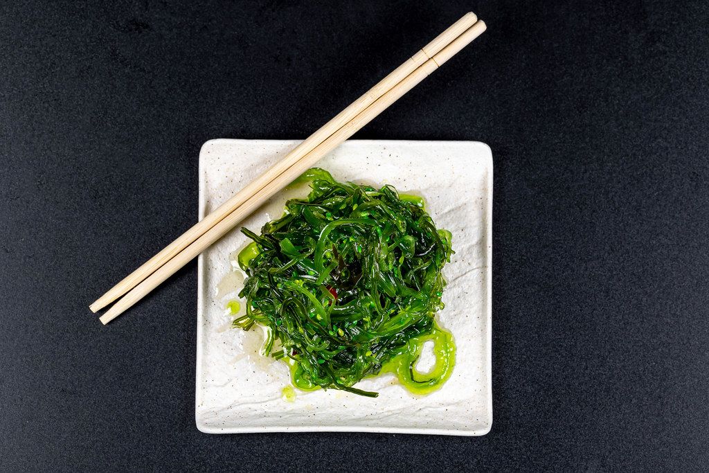 Top view, white plate with healthy seaweed salad on black background