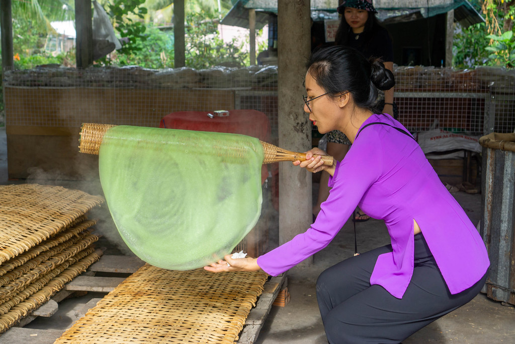 Touristin platziert ein handgemachtes Reispapiert auf einer Bambusliege in einem lokalen Workshop im Mekong Delta in Can Tho, Vietnam