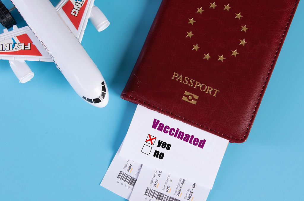 Traveling during COVID-19 virus, passport with airline ticket, covid-19 vaccinated card with "Yes" mark and plane on blue background